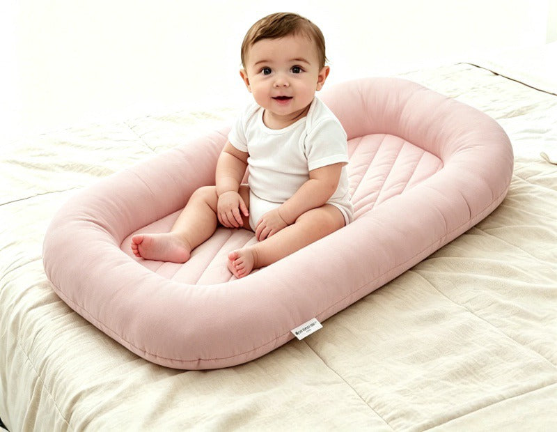 Baby sitting upright inside the Both Hands Baby Lounger placed on a bed