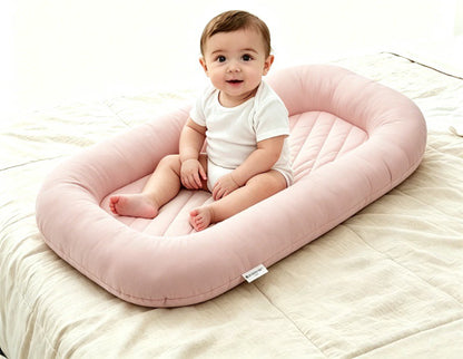 Baby sitting upright inside the Both Hands Baby Lounger placed on a bed