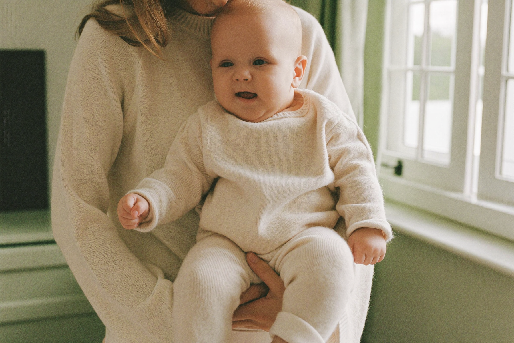 A mother holding her smiling baby by a bright window