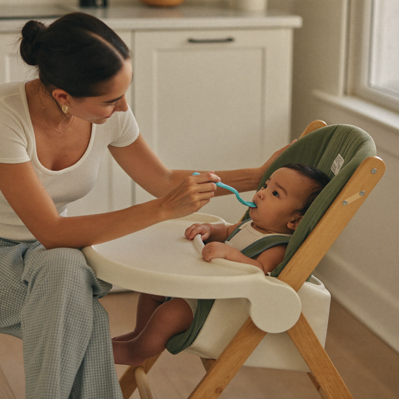 A parent feeding a happy baby in a high chair