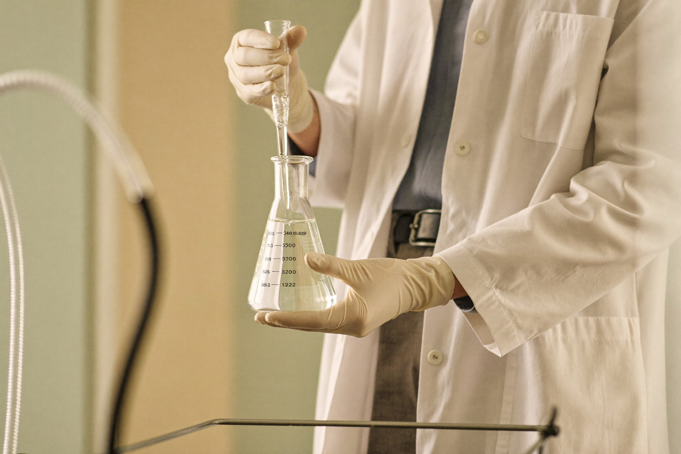 Gloved hands holding a glass beaker and pipette in a bright laboratory
